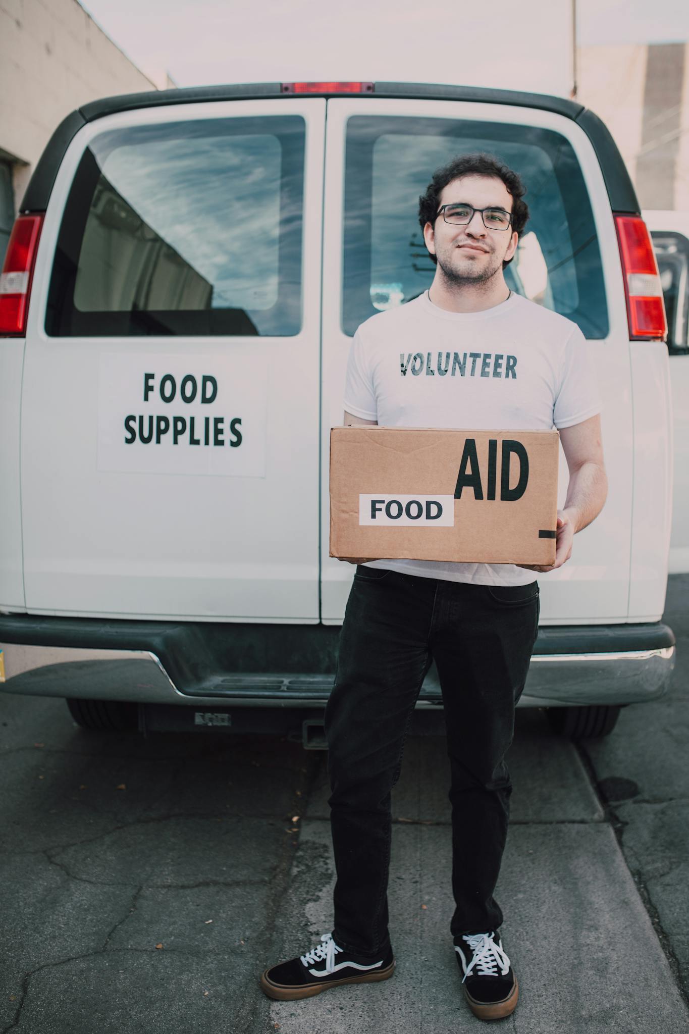 Volunteer standing in front of food supplies van with aid box, supporting community.